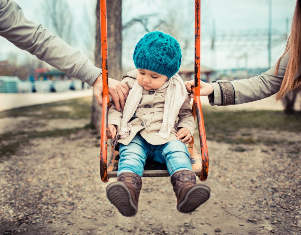 Couple pushing a young child on a swing.